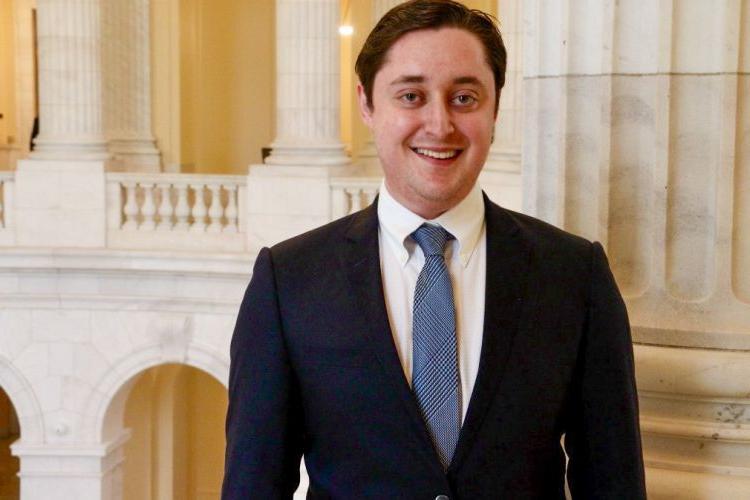 Man in black suit, blue tie, and white under shirt smiles for a headshot.